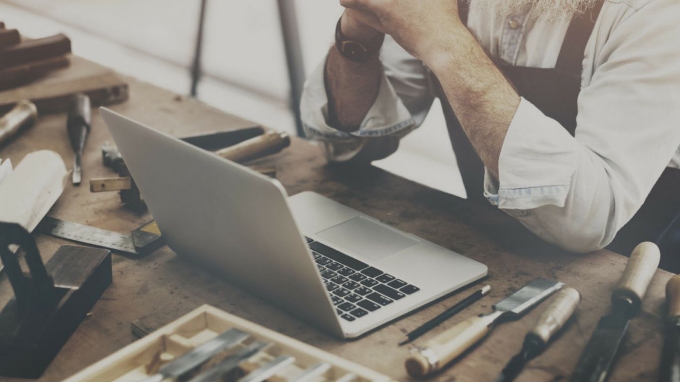 Handwerker mit Laptop und Werkzeug an der Werkbank